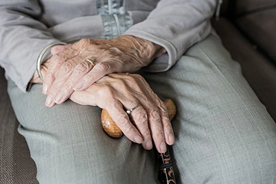 The hands of an old lady sat down, placed on top of each other with a walking stick